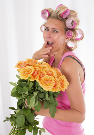 blond woman with pink curlers is holding a bouquet of rosesの写真素材