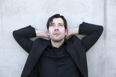 businessman is resting outdoors by leaning on a wall and looking up to the skyの写真素材
