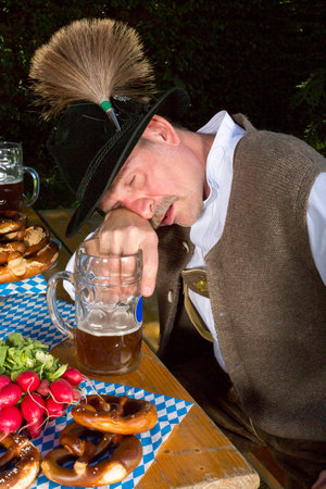 bavarian man sitting on bench with a beer mug and is drunkの写真素材