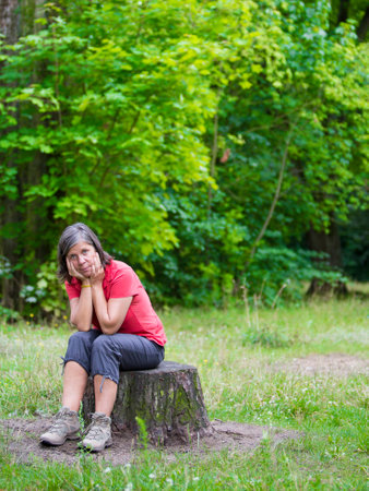 older woman sitting on a tree stump and looking sadの写真素材