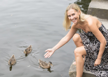 blond woman sitting by the water with ducksの写真素材
