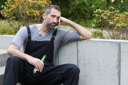workman sitting outside with a bottle of beer and sleeping
