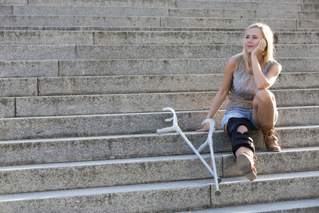 blonde woman with crutches sitting on stairsの写真素材