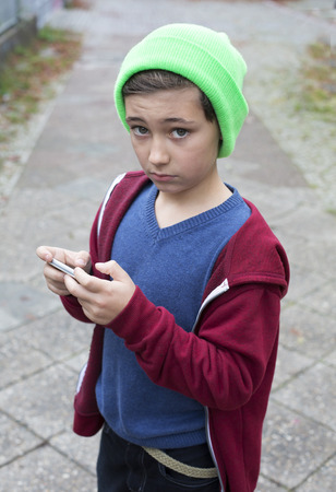 young boy standing outside and holding a phoneの写真素材