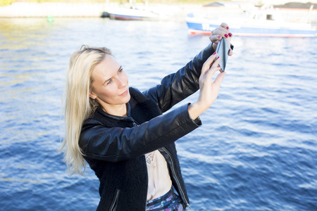 blond woman by the waterfront taking a selfieの写真素材