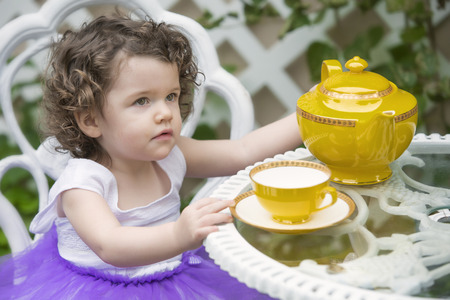 pretty little girl sitting in garden with cup and teapotの写真素材