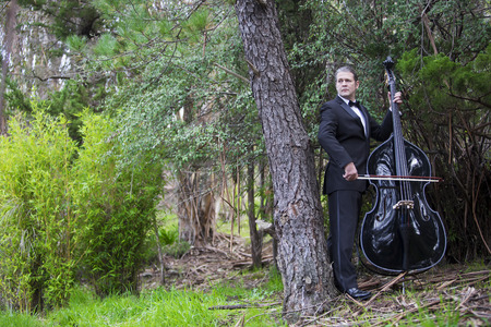 man in tuxedo playing the double bass in park