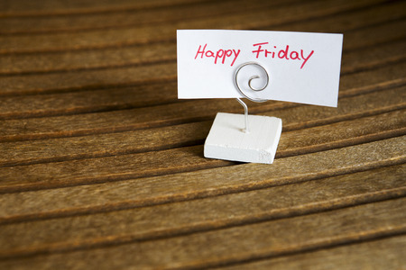 handwritten \\\ "happy friday \\\" on paper clipped on a stand on wood