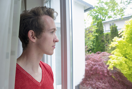 portrait of a young blond man looking out of a window