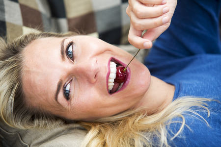 portrait of blond woman lying on couch and eating cherriesの写真素材