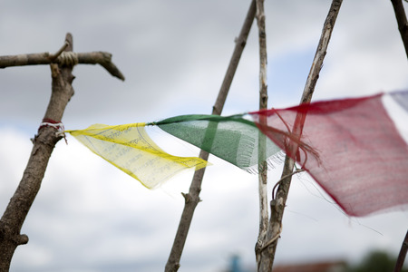 colorful buddhist prayer flags flying in front of cloudy sky on wooden sticks