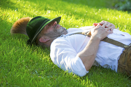 man in traditional bavarian clothes sleeping outside in the grassの写真素材