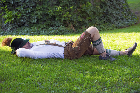 man in traditional bavarian clothes sleeping outside in the grassの写真素材