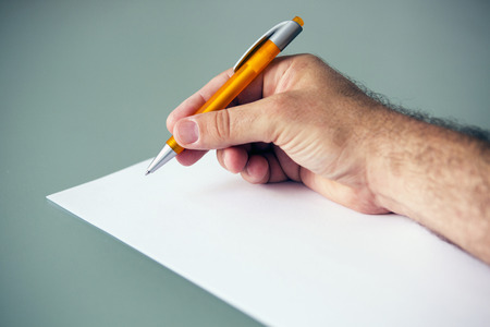 closeup of a man's hand holding a pen and a piece of white paper on tableの写真素材