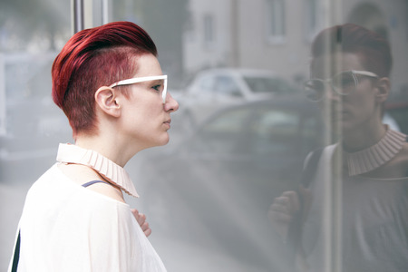 red-haired woman standing in front of a window and seeing her reflectionの写真素材