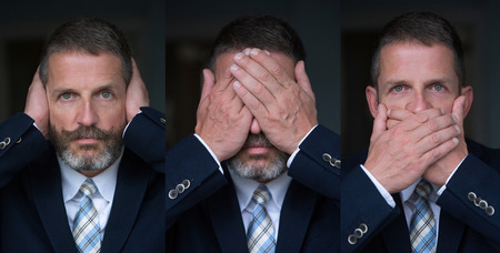 handsome man with beard and in suit and tie posing as the three wise monkeysの写真素材