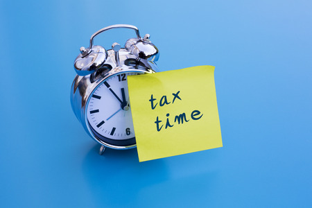 alarm clock on blue table with sticky note 'tax time'