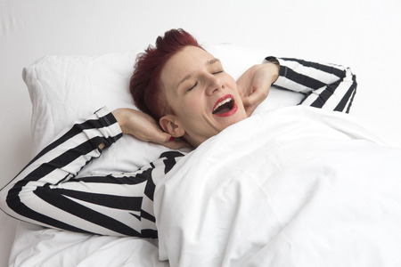 red-haired woman waking up in the morning and stretching and yawning