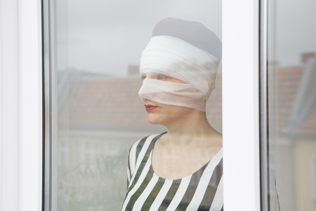 woman with bandages wrapped around her head looking out of a windowの写真素材