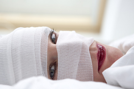 closeup of beautiful woman in bed with bandages wrapped around her headの写真素材
