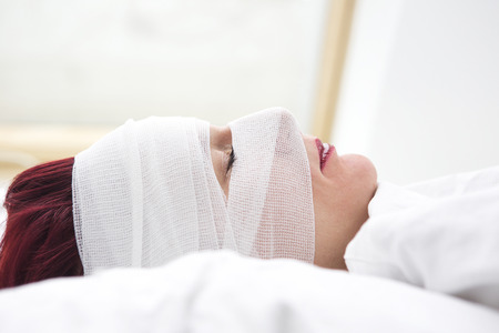 closeup of beautiful woman in bed with bandages wrapped around her headの写真素材