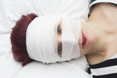 closeup of beautiful woman in bed with bandages wrapped around her headの写真素材