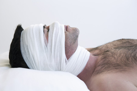 man in bed with bandages wrapped around his headの写真素材