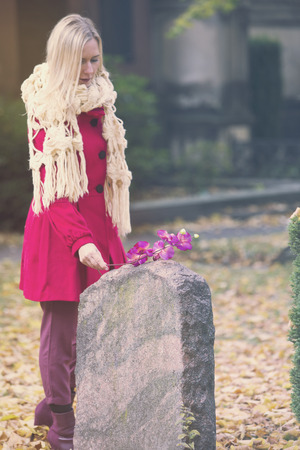 woman in autumn putting a flower at a tombstoneの写真素材