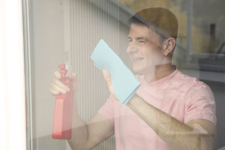 handsome man cleaning a window and smilesの写真素材