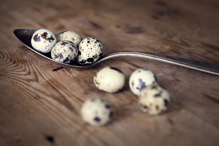 old silver spoon with quail eggs on wooden tableの写真素材