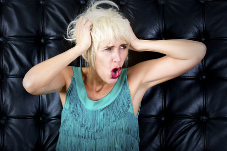 blond woman in green dress screaming in front of a black leather wallの写真素材