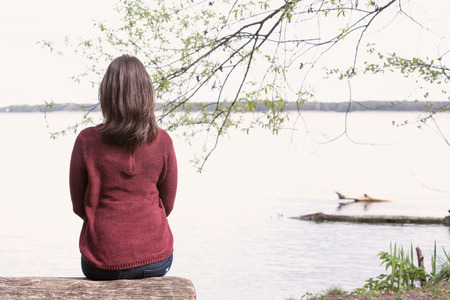 backside of brunette young woman sitting on tree in front of a lakeの写真素材