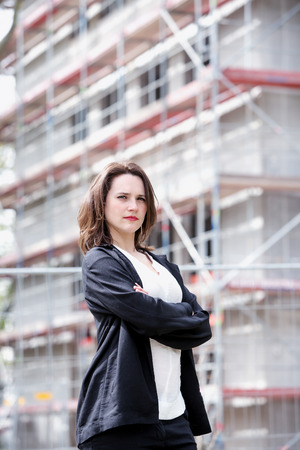 young businesswoman standing in front of construction site and looking at cameraの写真素材