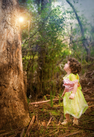 little girl in forest dressed as a fairy looking at a lightの写真素材