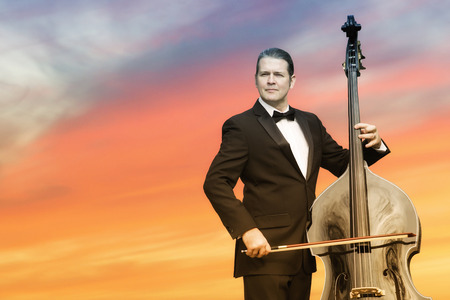 man in tuxedo playing the double bass in front of sunsetの写真素材