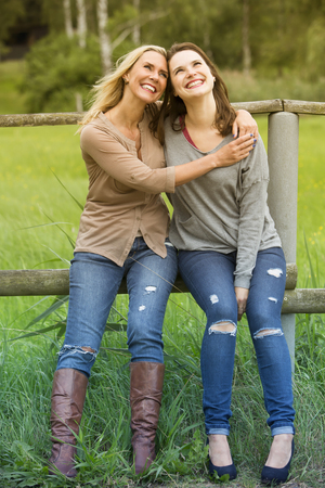 two woman hugging each other and sitting on fence outdoorsの写真素材