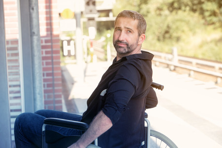 handsome man in his 40s sitting in wheelchair at train stationの写真素材