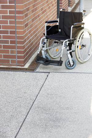 wheelchair standing by a brick wall on a sidewalkの写真素材