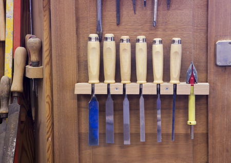 carving knives and screwdrivers hanging on wooden wall at workshop