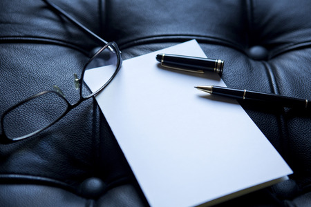 closeup of white paper and a stylish pen and eyeglasses on black leatherの写真素材