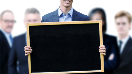 young businessman holding up a chalkboard with a group of businesspeople behind himの写真素材