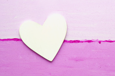 white wooden heart lying on a pink canvas