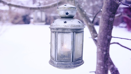 old rustic lantern with burning candle hanging on tree in the snowの写真素材