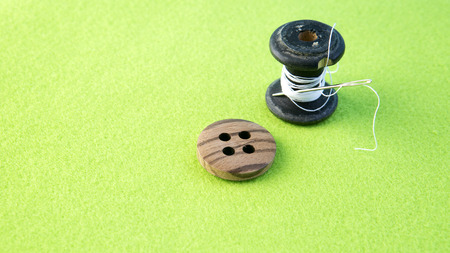 roll of yarn with button and needle on green table