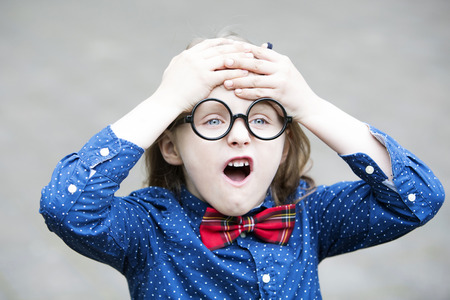 portrait of blond boy with bow tie and big glasses looking upsetの写真素材