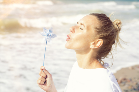 beautiful blond woman sitting on the beach with a pinwheelの写真素材