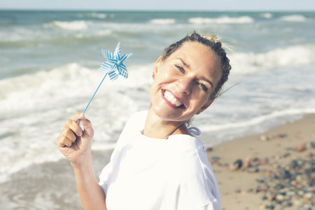 beautiful blond woman sitting on the beach with a pinwheelの写真素材