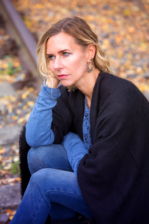 blond woman sitting outside on trail tracks and looking sadの写真素材