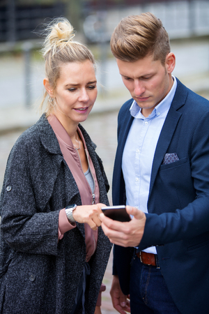 man and woman standing in the street and looking at phoneの写真素材