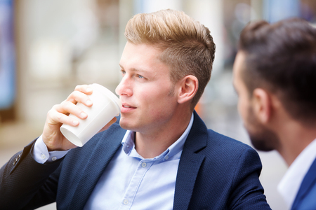 portrait of two handsome businessmen outside while one is drinking from a cupの写真素材